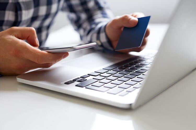 Person holding card and mobile in front of laptop