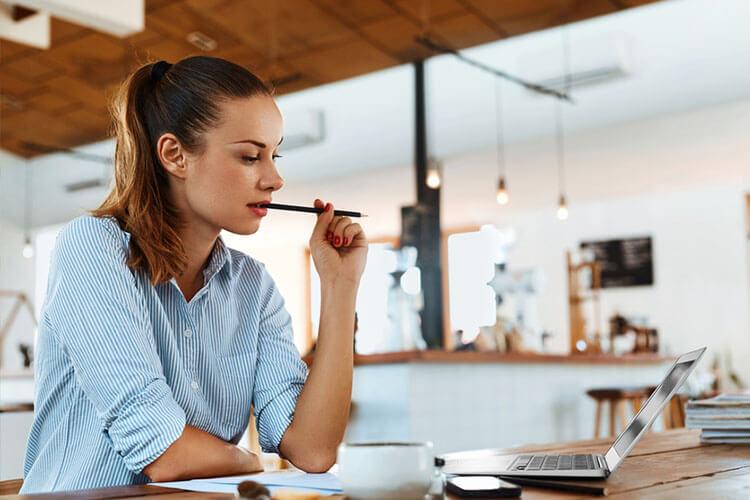 Woman with pen in mouth looking at laptop